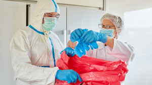 Cleaning professionals wearing PPE disposing of gloves into biohazard bag during needle sweep service