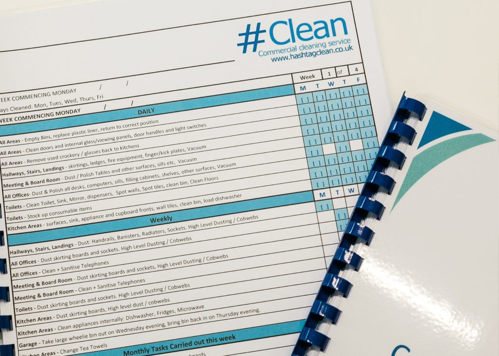 Close-up of a Hashtag Clean office cleaning checklist detailing daily and weekly office cleaning tasks, with a branded spiral-bound folder partially visible.