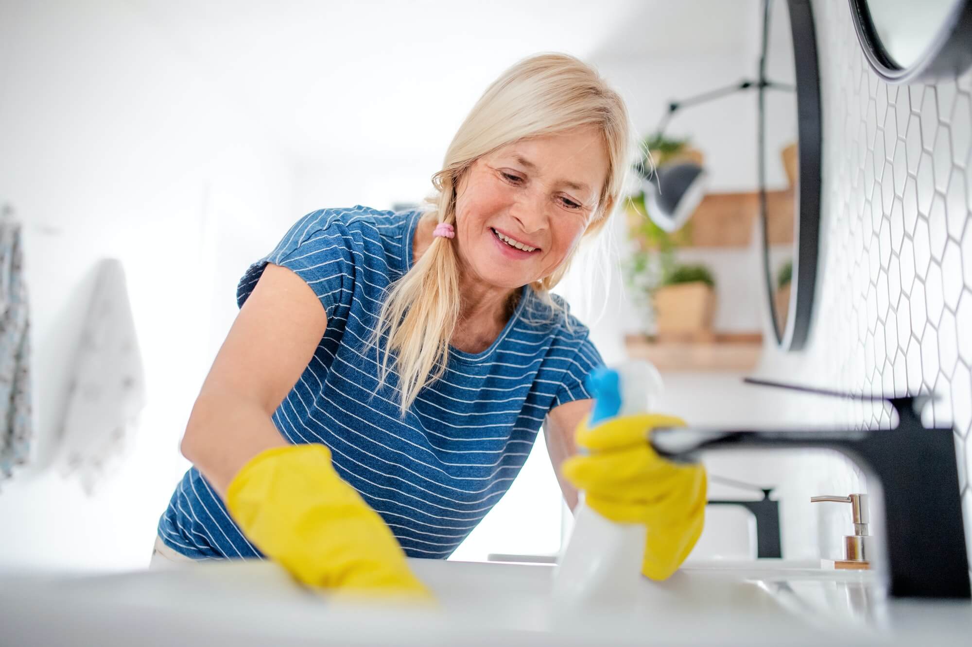 Senior Woman With Gloves Cleaning Bathroom Indoors At Home