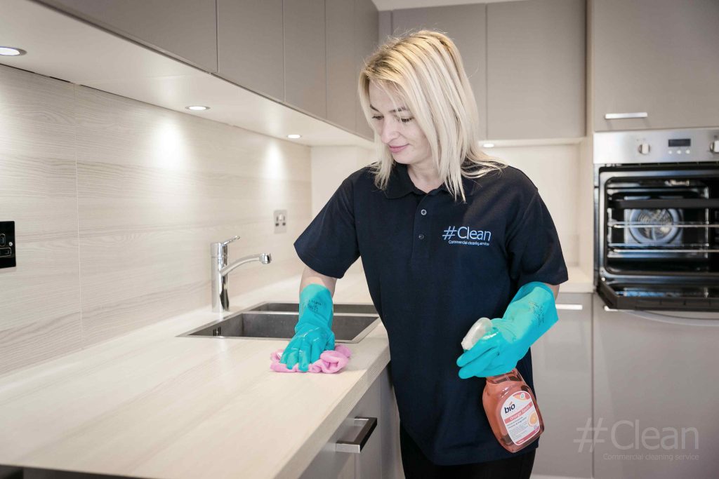 woman in hashtag clean uniform wiping a kitchen counter clean